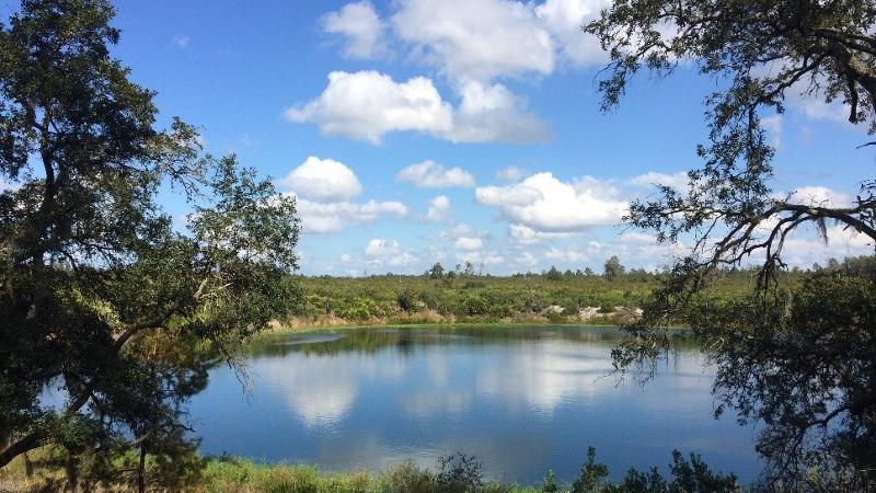 a blue lake surrounded by green trees mirrors the cloudy sky above it.